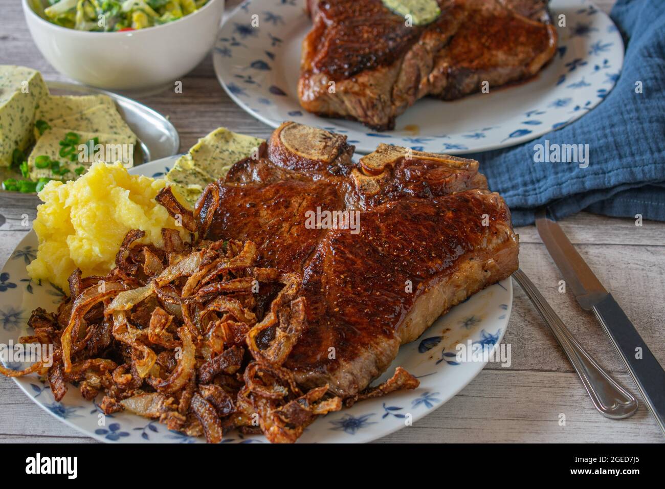 T-Bone irlandese biologico e stagionato a secco o bistecca di porterhouse con cipolle fritte, purè di patate e insalata su un piatto Foto Stock