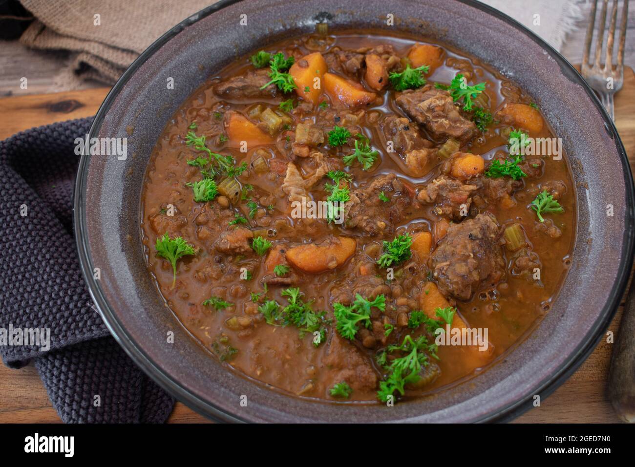 Stufato di manzo con lenticchie e verdure servito in una rustica ciotola di smalto su tavola di legno. Foto Stock