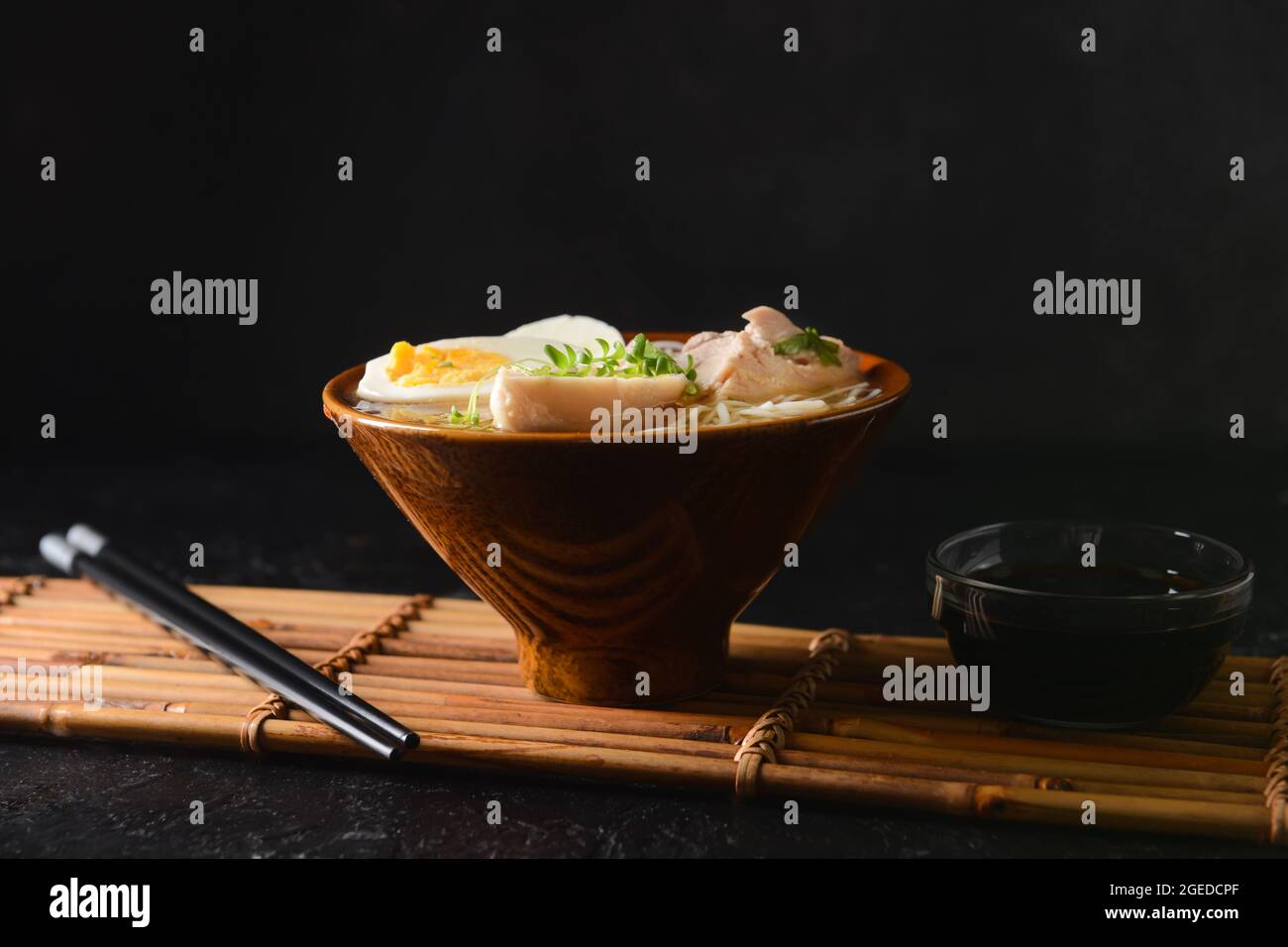 Gustosa zuppa cinese con pollo in ciotola con salsa di soia su fondo scuro Foto Stock