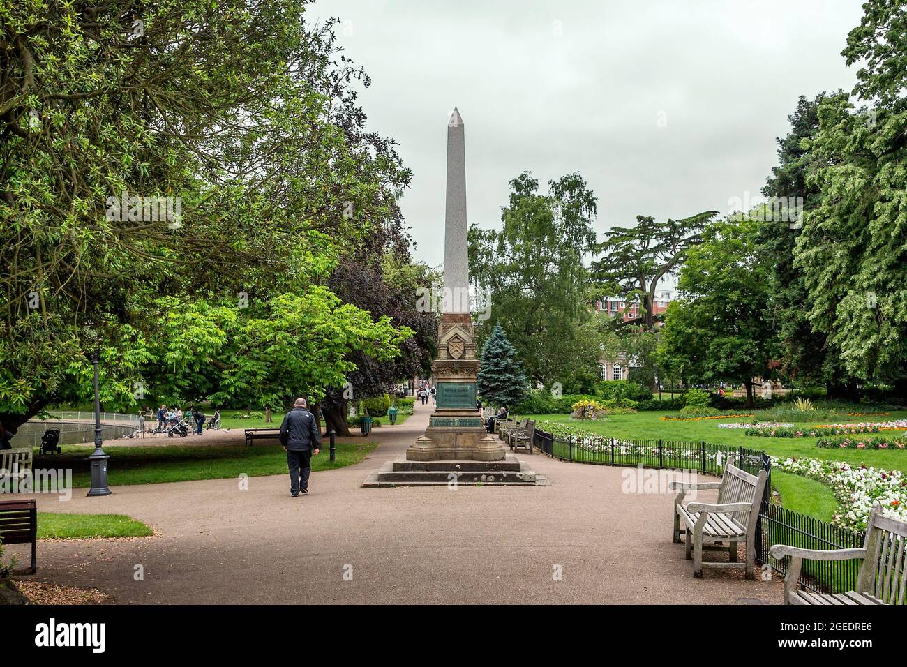 La gente gode di una passeggiata attraverso i Giardini di Jephson e la Royal Leamington Spa. L'obelisco di Willes, un obelisco di granito con un piedistallo neogotico, si erge al centro. Foto Stock