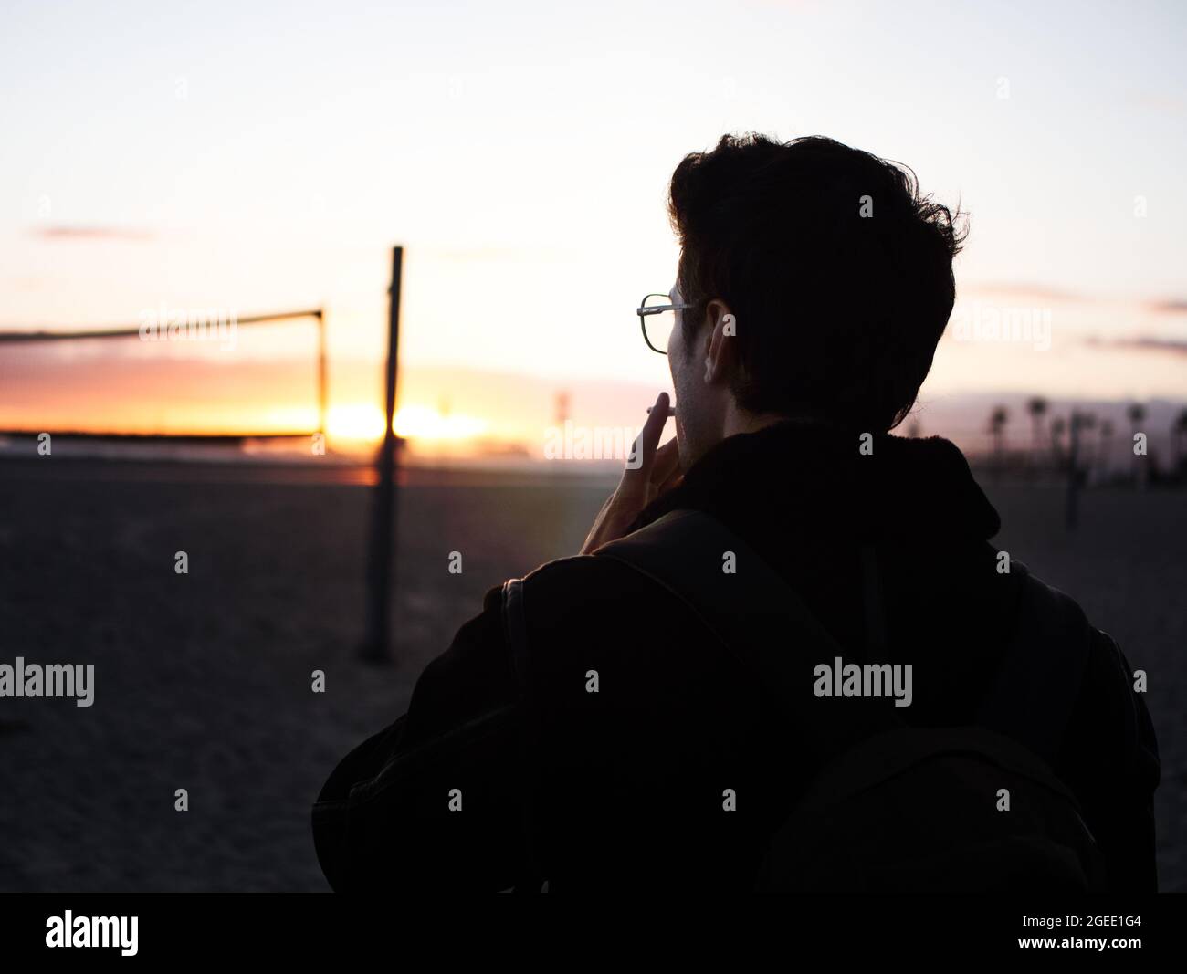 Un bel giovane in spiaggia al tramonto fumando Foto Stock