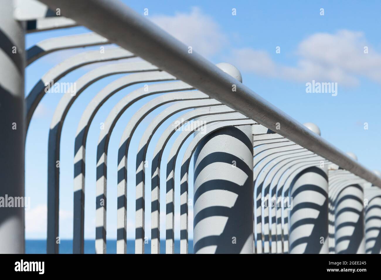 Dettagli astratti di architettura contemporanea, struttura di ringhiere metalliche con motivi d'ombra sotto il cielo blu nuvoloso Foto Stock