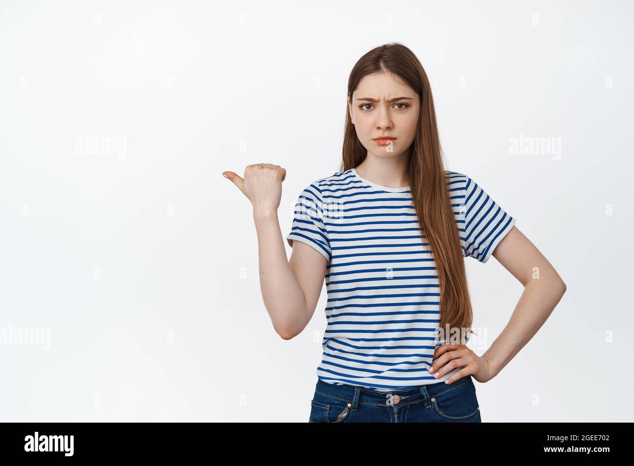 Ritratto di ragazza arrabbiata che punta a sinistra, offuscando deluso, lamentandosi di smth, in piedi su sfondo bianco Foto Stock