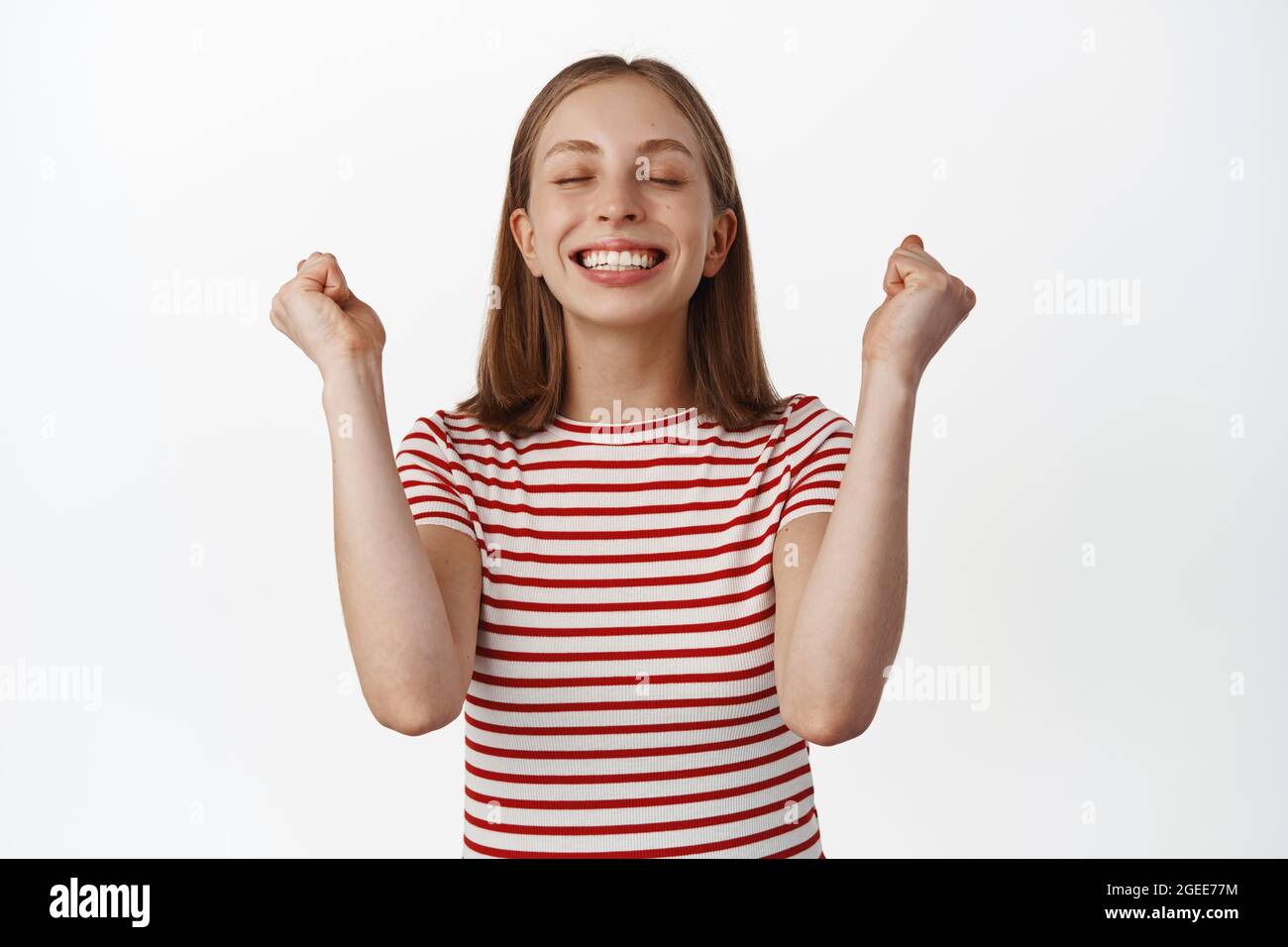 Ragazza bionda felice e sollievo gioendo dalla vittoria, raggiungere l'obiettivo, soddisfatto del risultato, pompa pugnale con occhi chiusi, sorridente denti bianchi, trionfante Foto Stock