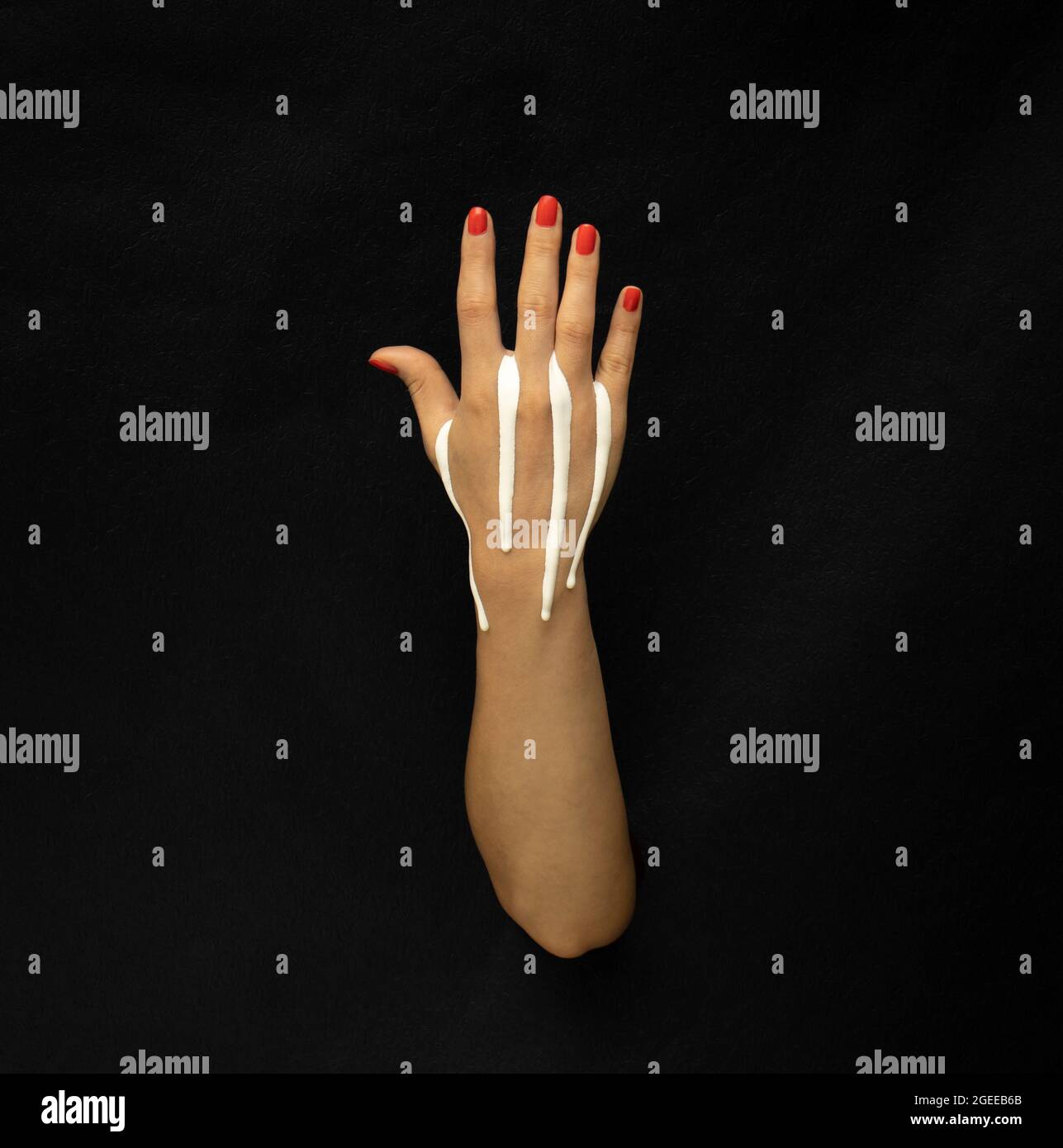 Strisce bianche di vernice che gocciolano lungo la mano aperta su sfondo nero. Foto Stock