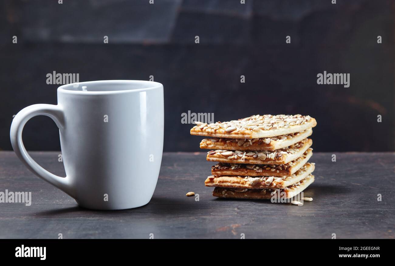 Tazza bianca con caffè e croccante croccante su sfondo di legno, primo piano. Colazione gustosa, concetto di routine mattutino Foto Stock