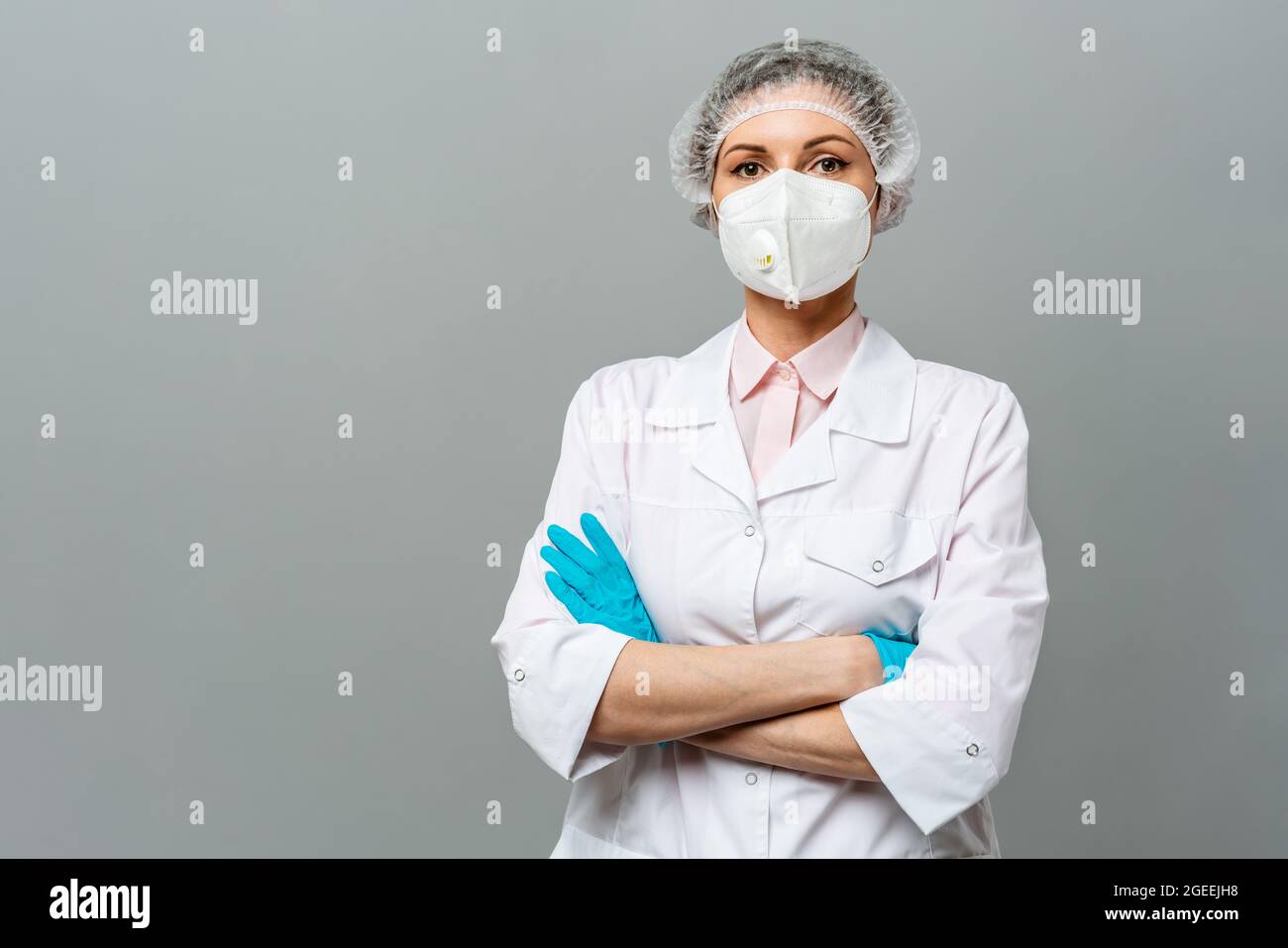 Ritratto di una giovane donna infelice medico in una maschera medica su sfondo grigio. Gli occhi stanchi del medico. Il concetto di coronavirus. Foto Stock