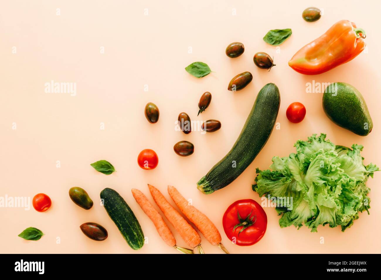 Zucchine, avocado, pomodoro, carota, cetriolo, peperone e lattuga su sfondo beige. Cibo vegano crudo sano, dieta, concetto di disintossicazione. Vista dall'alto, piatta Foto Stock