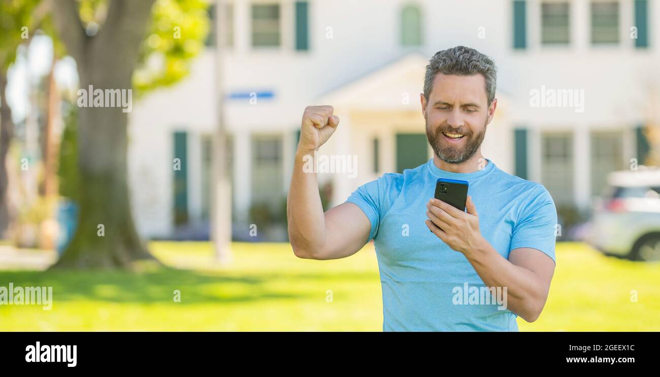 uomo maturo felice in piedi all'aperto a casa lettura messaggio su smartphone, immobiliare Foto Stock