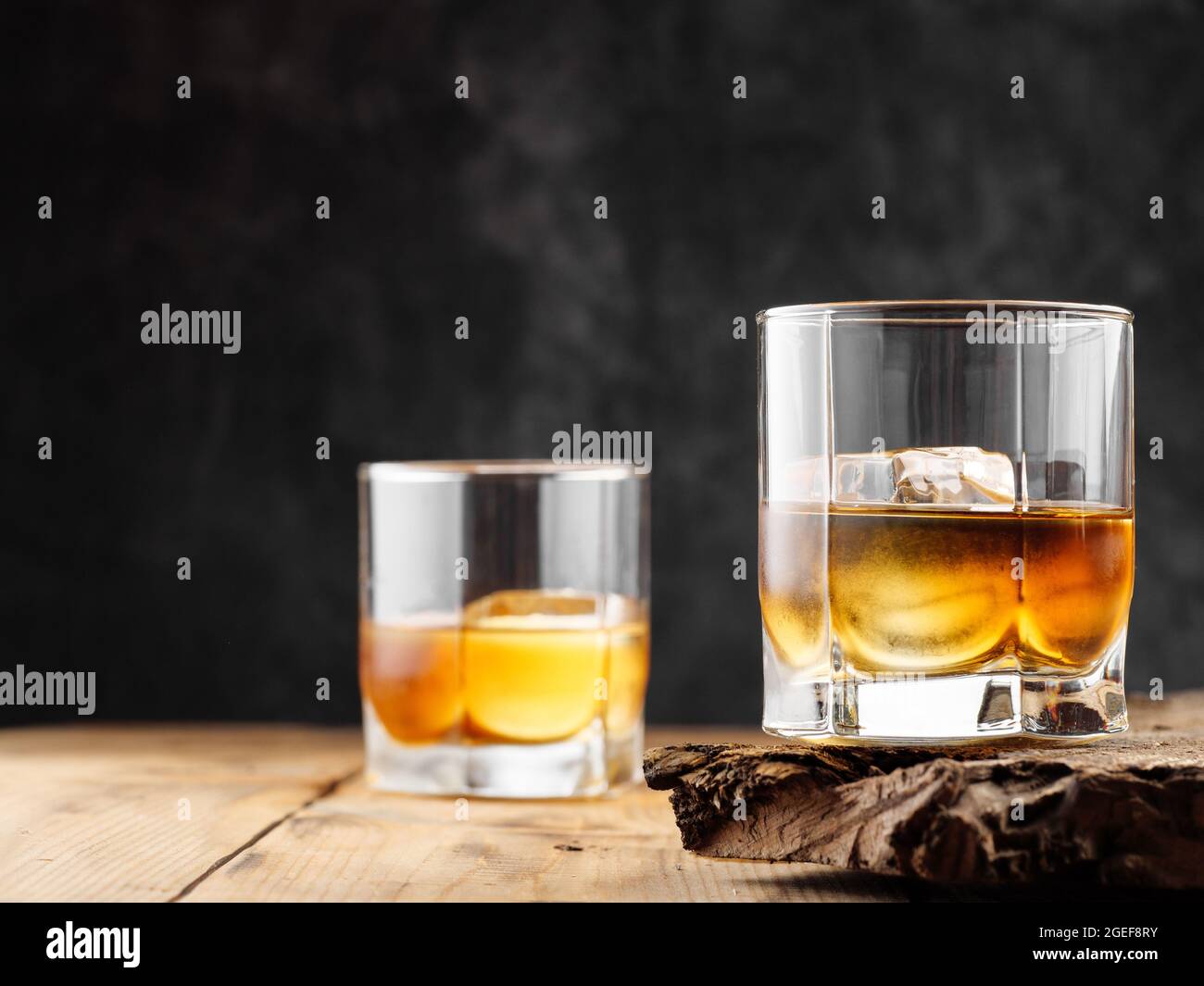 Due bicchieri con cubetto di ghiaccio e whiskey su un vecchio tavolo di legno. Spazio di copia. Foto Stock