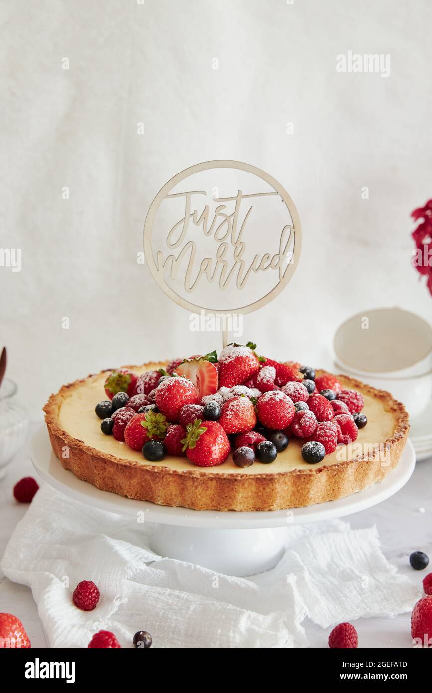 Deliziosa cheesecake con frutti di bosco freschi in cima e un topper che dice appena sposato Foto Stock