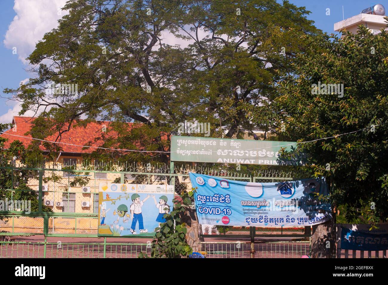 Una scuola primaria chiusa appende un COVID bilingue - 19 banner accanto a un cartello dipinto a mano all'ingresso della scuola. Le scuole sono state chiuse a Phnom Penh per oltre 5 mesi a causa della pandemia del coronavirus. Phnom Penh, Cambogia. 18 agosto 2021. © Kraig Lieb Foto Stock