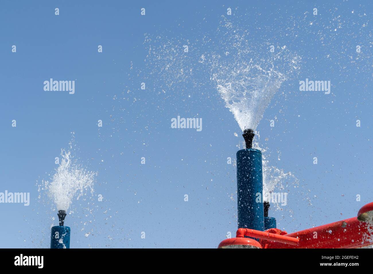 Due spruzzatori blu del parco acquatico spruzzano l'acqua nel cielo per il divertimento estivo dei bambini. Foto Stock