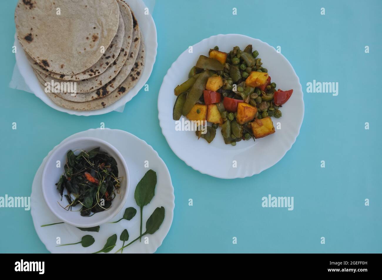 North Indian Food - Matar paneer mix di verdure, saag e roti su piastra bianca con sfondo azzurro Foto Stock