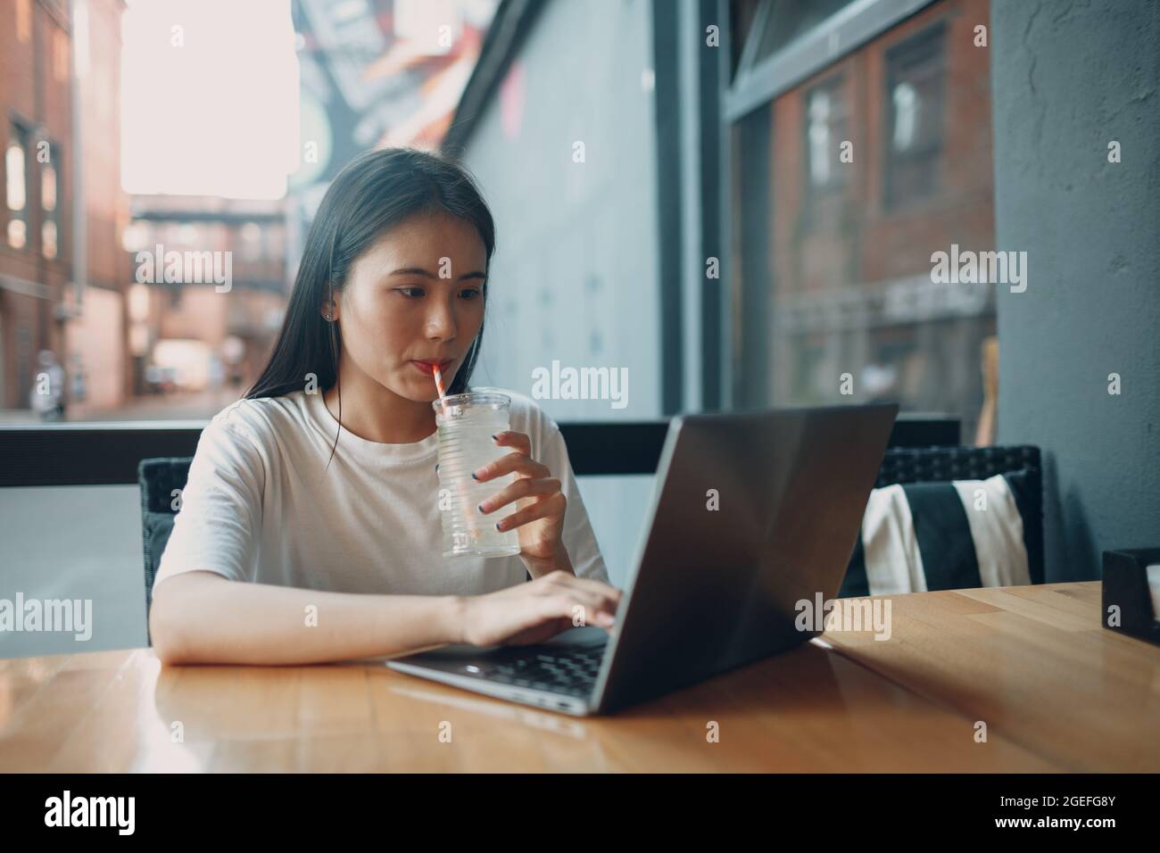 La giovane donna asiatica beve soda di limonata e usa un computer portatile al bar all'aperto. Foto Stock