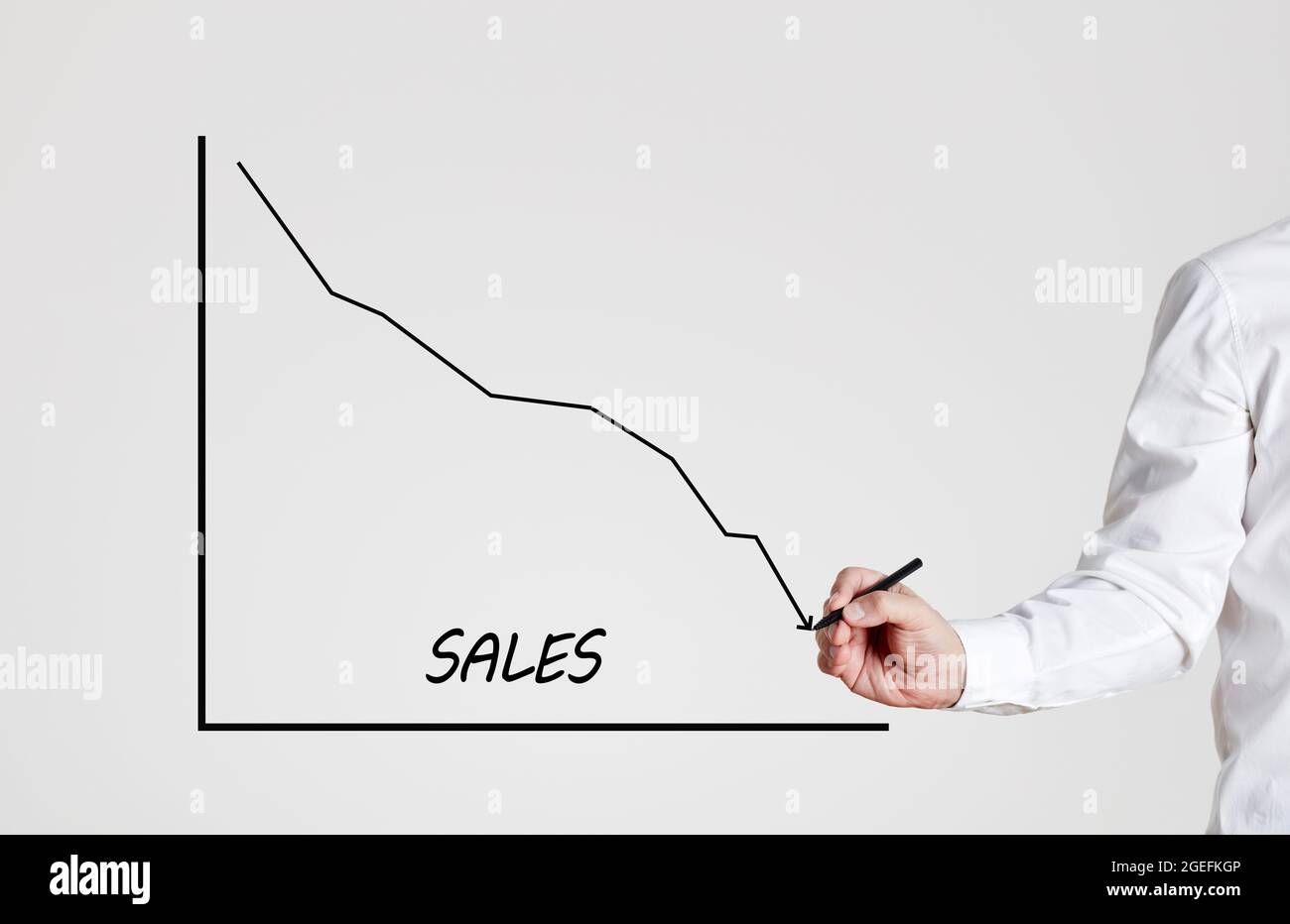 Businessman disegna un grafico di linea in declino con la parola vendite. Riduzione del concetto di vendita. Foto Stock