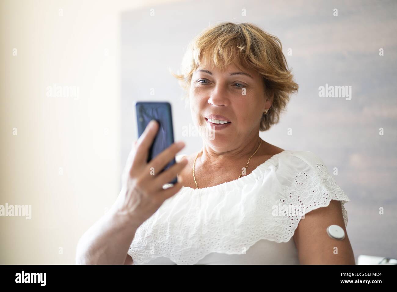 Donna che verifica il livello di glucosio con il monitoraggio continuo del glucosio su dispositivi mobili Telefono Foto Stock