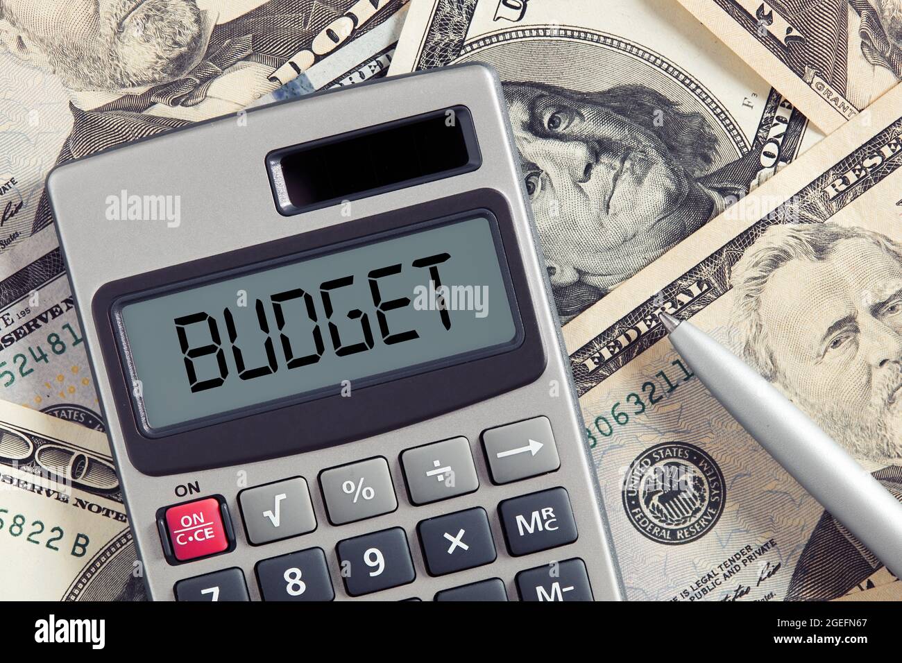 La parola budget sul display della calcolatrice con sfondo bollette in dollari. Analisi o pianificazione del budget, concetto di finanza aziendale. Foto Stock