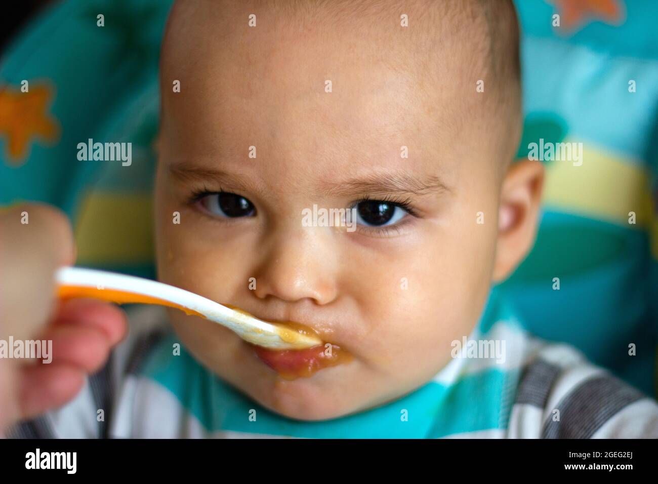 Il bambino divertente arrabbiato è alimentato a cucchiaio. Madre che alimenta il suo bambino con verdure di purea Foto Stock