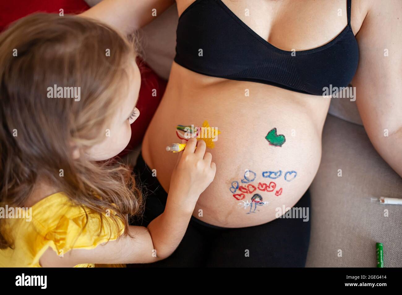 Carino piccola figlia dipinto su donna incinta pancia Foto Stock