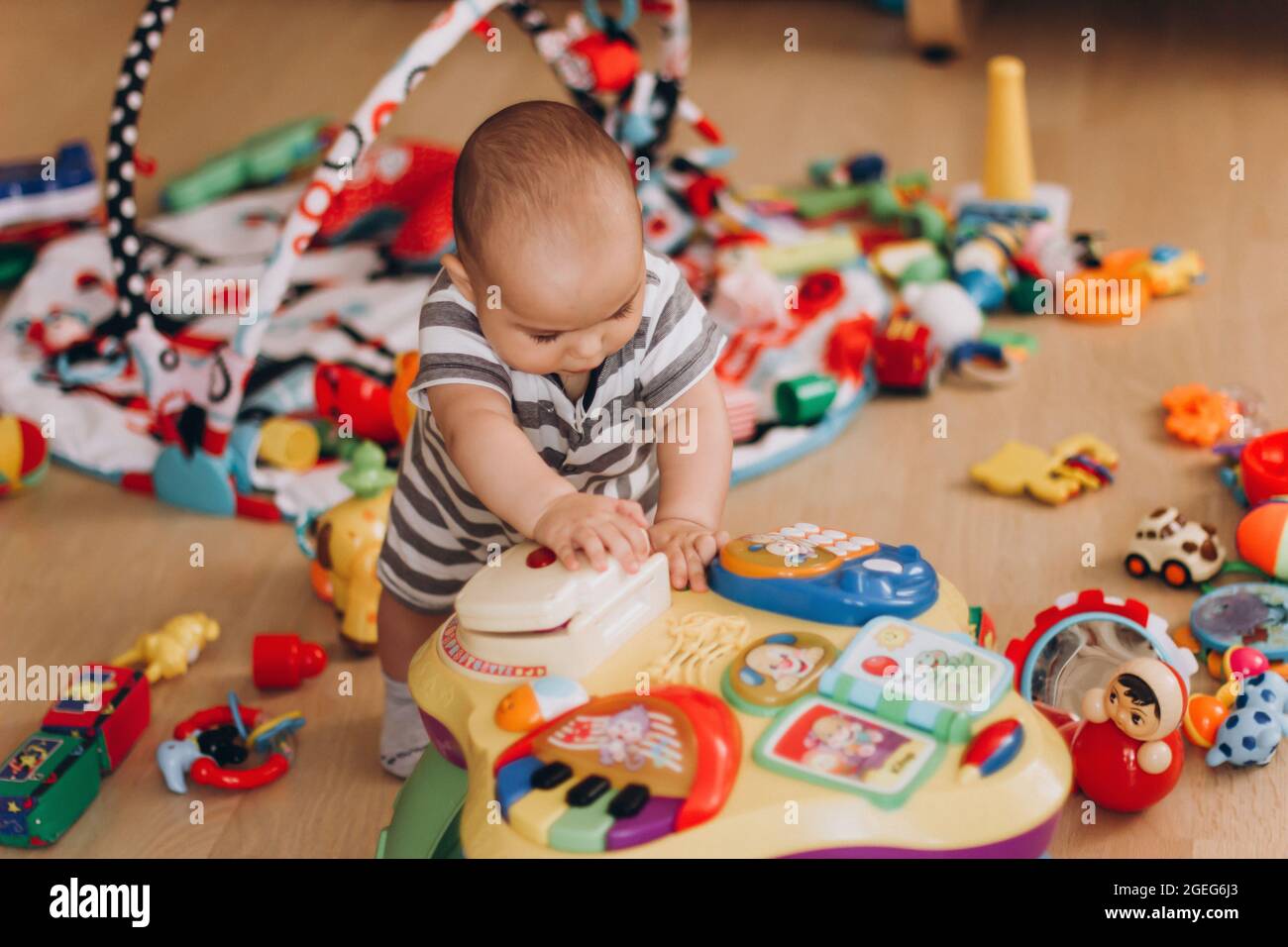 Simpatico baby chubby si alza e gioca con il tavolo di musica per bambini. Un sacco di giocattoli colorati ovunque. Foto Stock