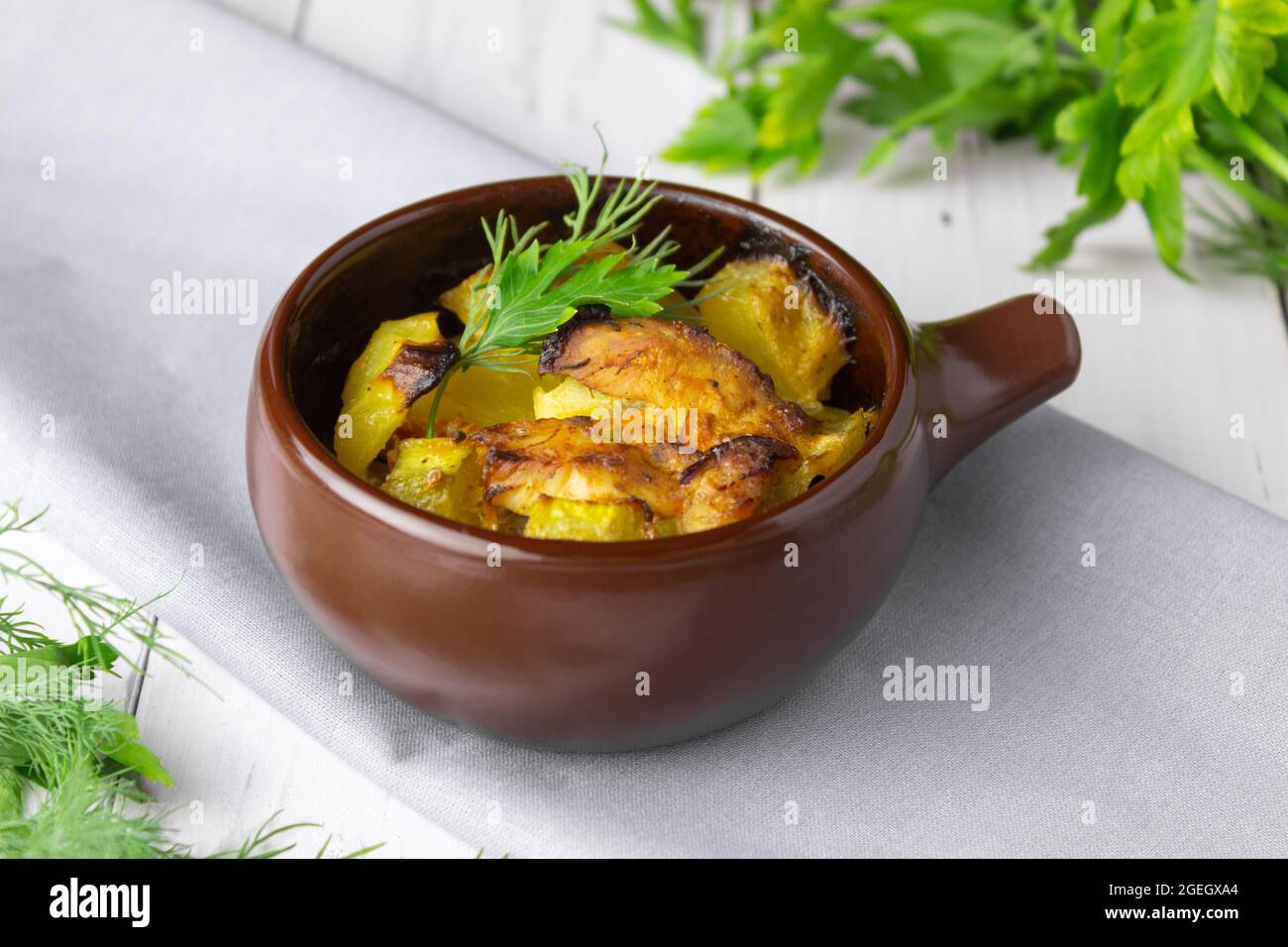 Patate, pollo e zucchine cotte in una pentola di argilla su sfondo chiaro. Foto Stock
