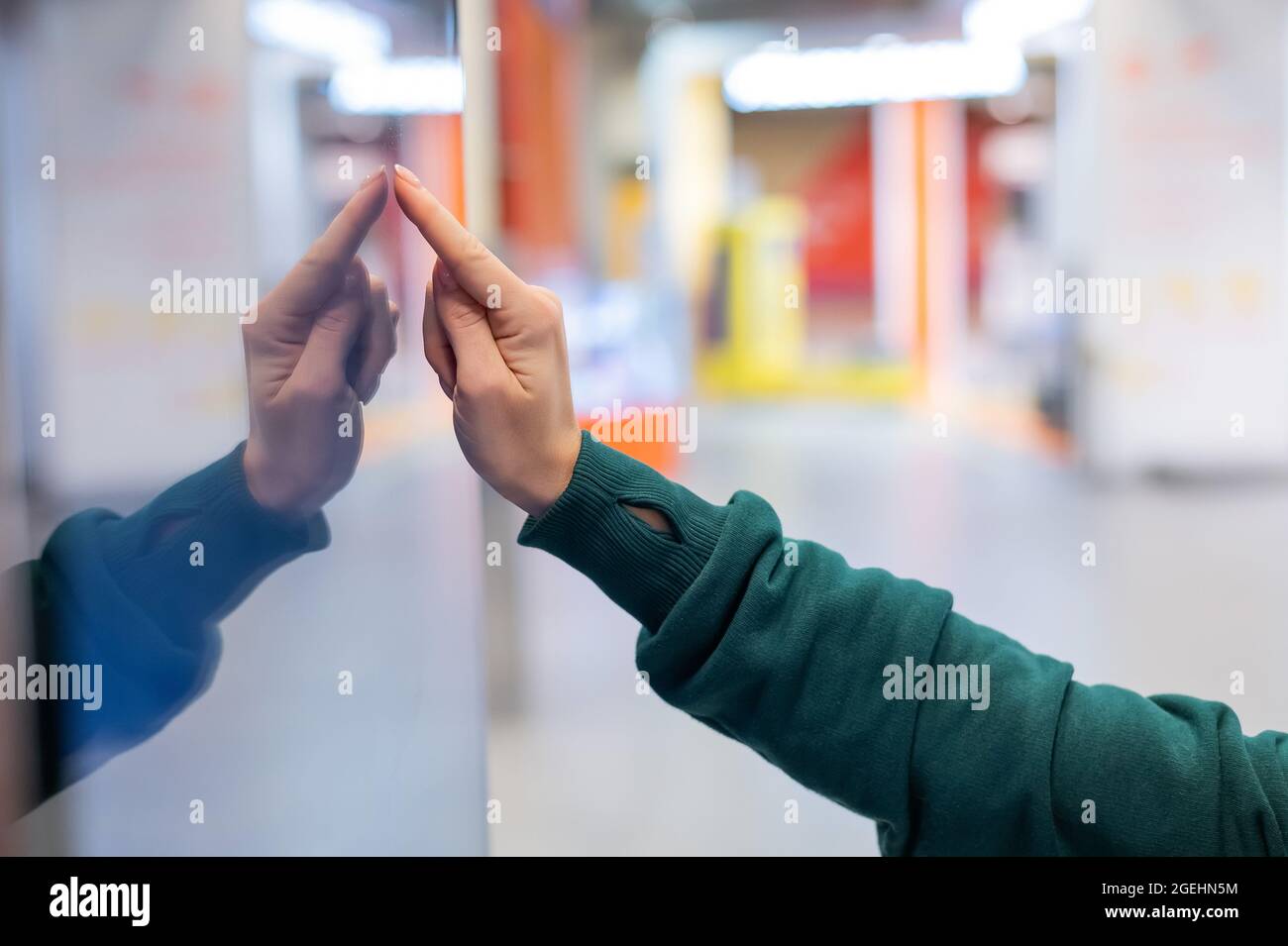 La donna senza volto in maschera medica utilizza la scheda elettronica di informazioni in un luogo pubblico Foto Stock