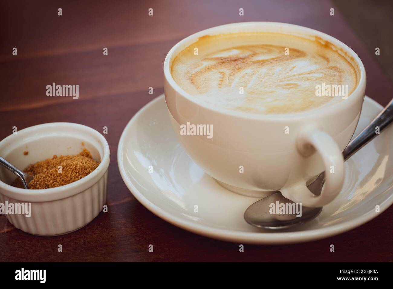 caffè con latte schiumato con grande foglia modello, accanto ad esso è zucchero di canna crudo, fuoco selettivo sul centro della tazza Foto Stock