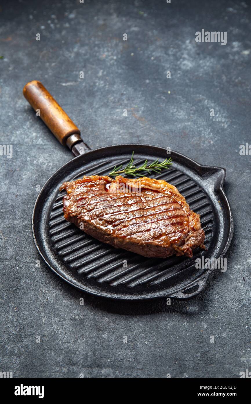 Bistecca di lombo fritta su una padella e posate vintage in ghisa, fondo nero. Vista dall'alto Foto Stock