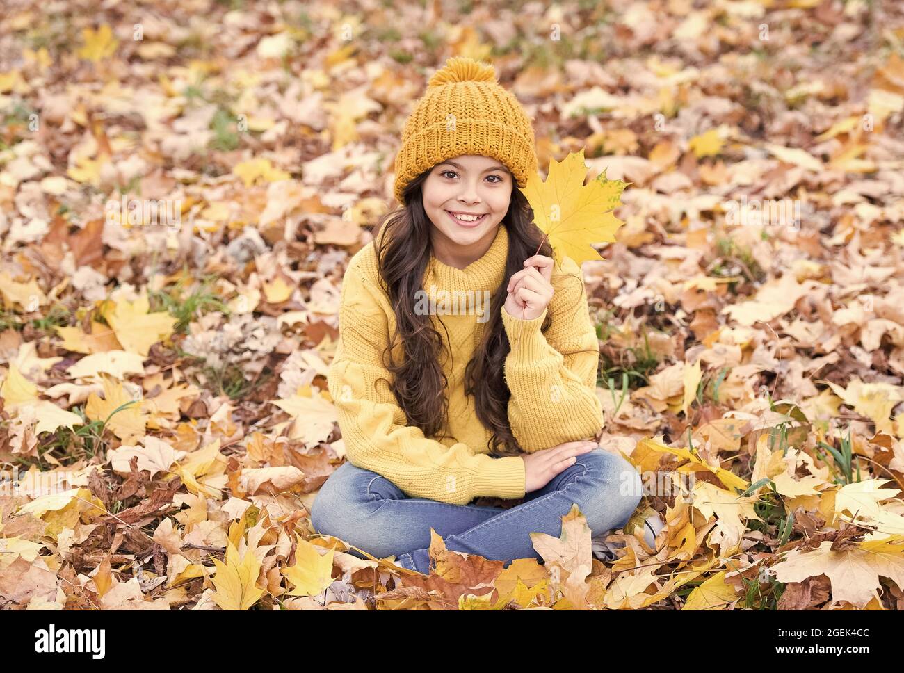 Girando una nuova foglia. Piccola ragazza felice il giorno d'autunno. Piccolo sorriso del capretto seduto sulle foglie di caduta. Piccolo bambino tenere foglia autunno. Adorabile bambino piccolo dentro Foto Stock