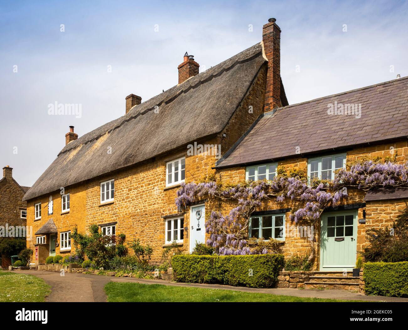 Regno Unito, Inghilterra, Oxfordshire, Wroxton, Main Street, Glicine in fiore sopra le porte di graziosi cottage in pietra di Cotswold Foto Stock