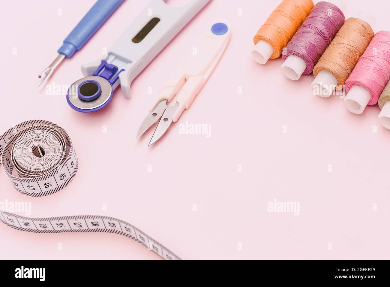 Fondo rosa con accessori per cucire e tessuto. Fili da cucire, aghi, tessuti, nastri da cucire al centimetro o di misura. Spazio di copia. Soppies sartoriali Foto Stock