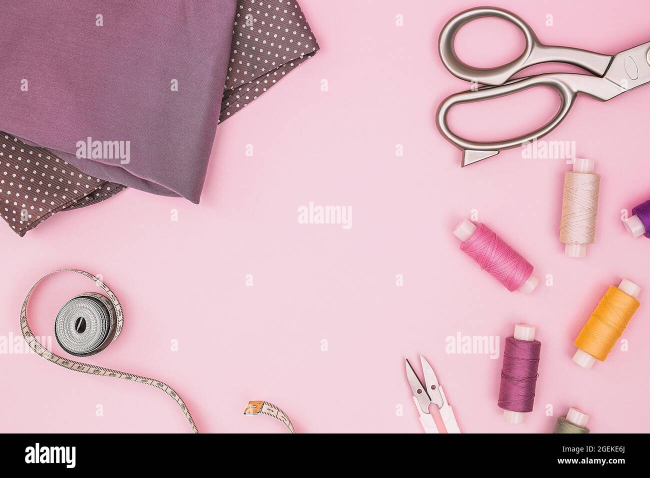 Fondo rosa con accessori per cucire e tessuto. Fili da cucire, aghi, tessuti, nastri da cucire al centimetro o di misura. Vista dall'alto, spazio di copia. Su misura Foto Stock