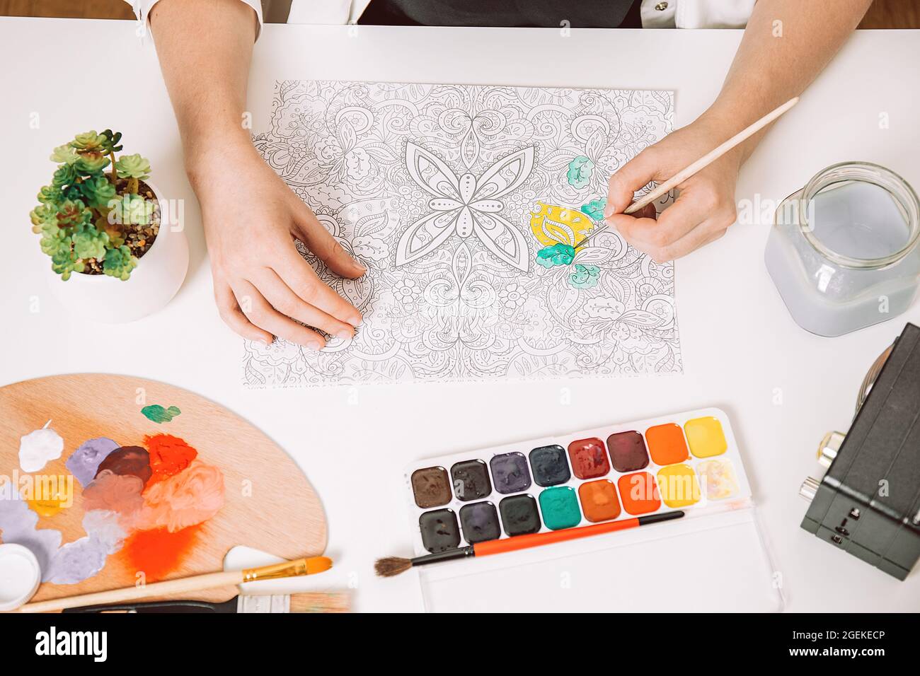 Terapia d'arte o autoespressione per adulti. La giovane donna sta colorando pagina anti libro di sforzo, concetto di benessere mentale. Spazio di lavoro dell'artista - Paints, penc Foto Stock