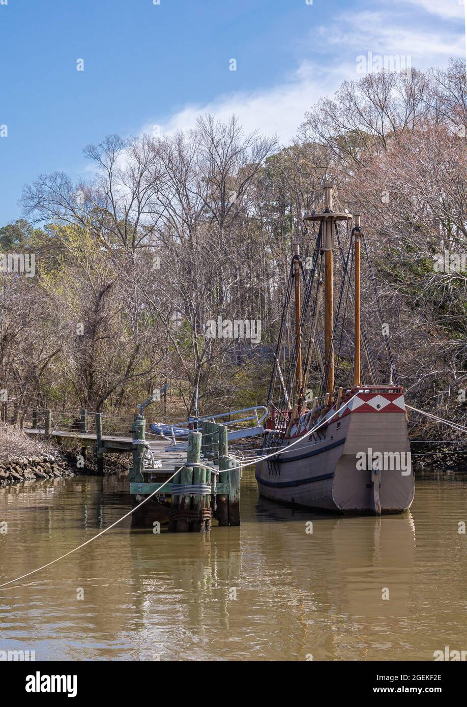 Jamestowne, VA, USA - 1 aprile 2013: Sito storico. Vecchia barca a vela ormeggiata sulle acque bruno del fiume Jamer con alberi senza foglie sul retro sotto la nuvola blu Foto Stock