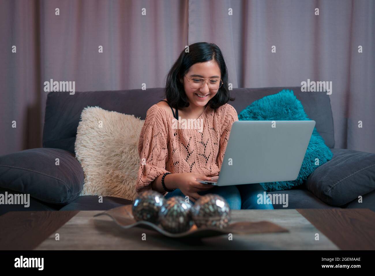 Vista orizzontale di un adolescente seduto sul divano con il suo laptop, presta attenzione e sorride alla videochiamata, prende classe virtuale Foto Stock