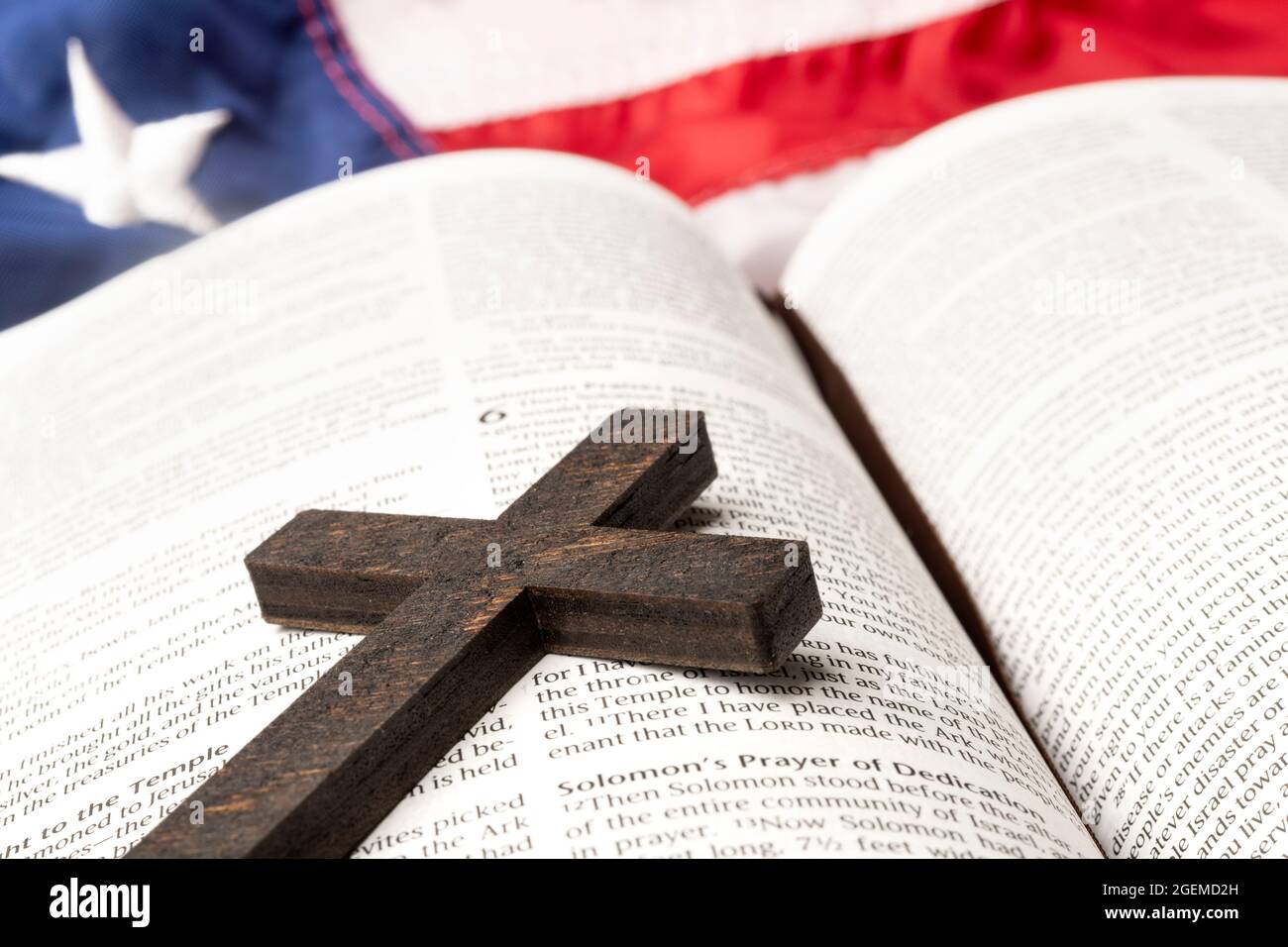 Una piccola croce di legno poggia su una bibbia con la bandiera americana sul tavolo. Foto Stock