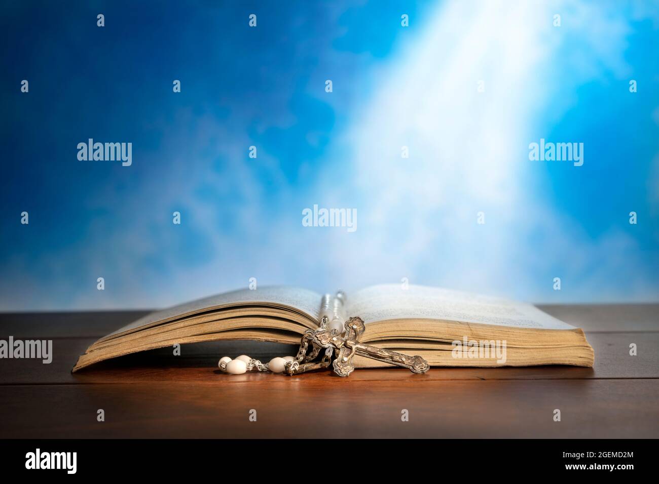 Immagine drammatica che mostra un fascio luminoso che brilla su una vecchia bibbia con un rosario che si posa davanti ad essa. Foto Stock