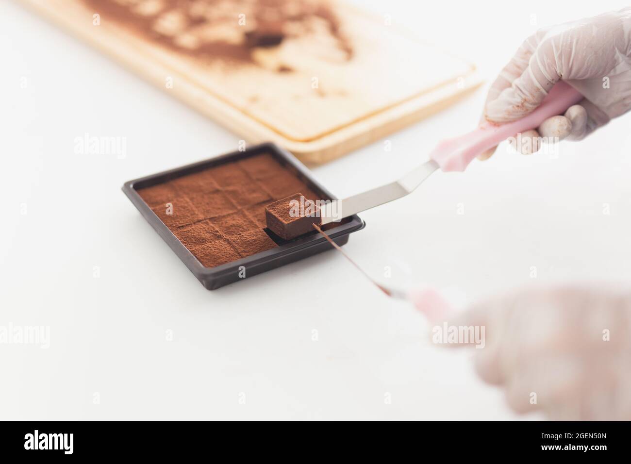 Chef mano con guanto che impacchettano il cioccolato Nama in una scatola. Foto Stock