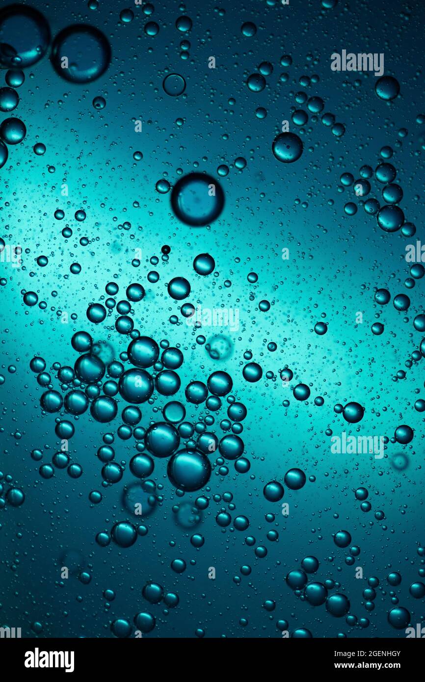 Scatti macro di gocce d'olio mescolate in acqua retroilluminata con luce blu Foto Stock