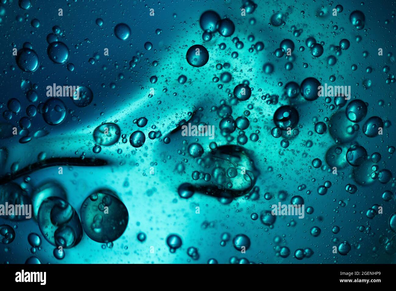 Scatti macro di gocce d'olio mescolate in acqua retroilluminata con luce blu Foto Stock