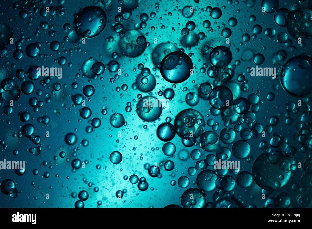 Scatti macro di gocce d'olio mescolate in acqua retroilluminata con luce blu Foto Stock