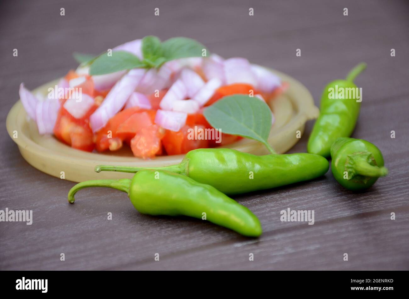closeup il pomodoro rosso affettato con cipolla, peperoncino verde e foglie di menta nel piatto di plastica su sfondo marrone fuori fuoco. Foto Stock