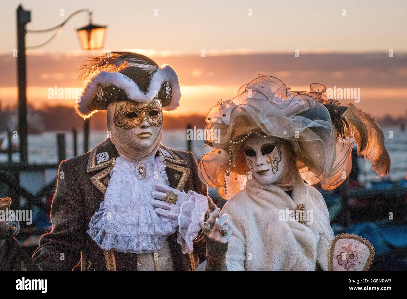 Maschio e femmina con maschere, cappelli e costumi di carnevale in piedi  accanto all'acqua al tramonto a Venezia Foto stock - Alamy
