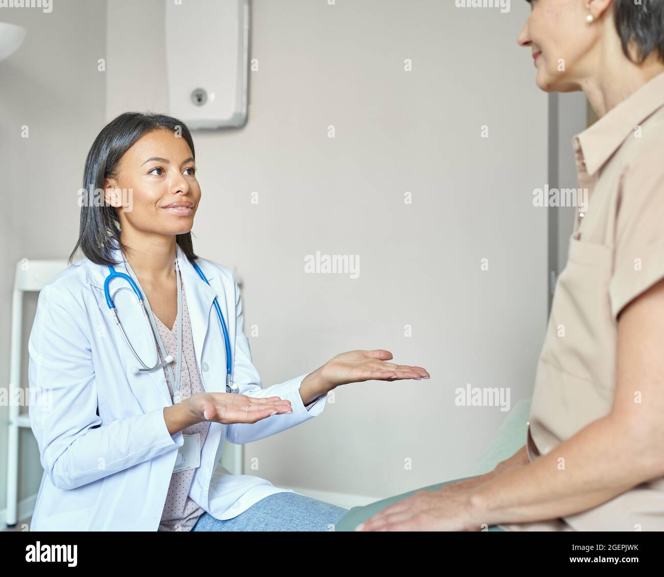 Giovane sostenente afro medico americano femmina raggiungere le mani per aiutare la paziente di mezza età Foto Stock
