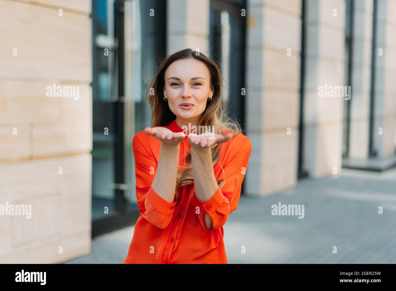 Donna di trent'anni sorride e mostra bacio d'aria con gesti delle mani Foto Stock