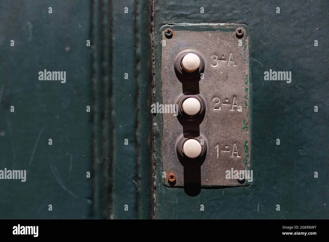 antico campanello con tre pulsanti su una porta di legno dipinta di verde Foto Stock
