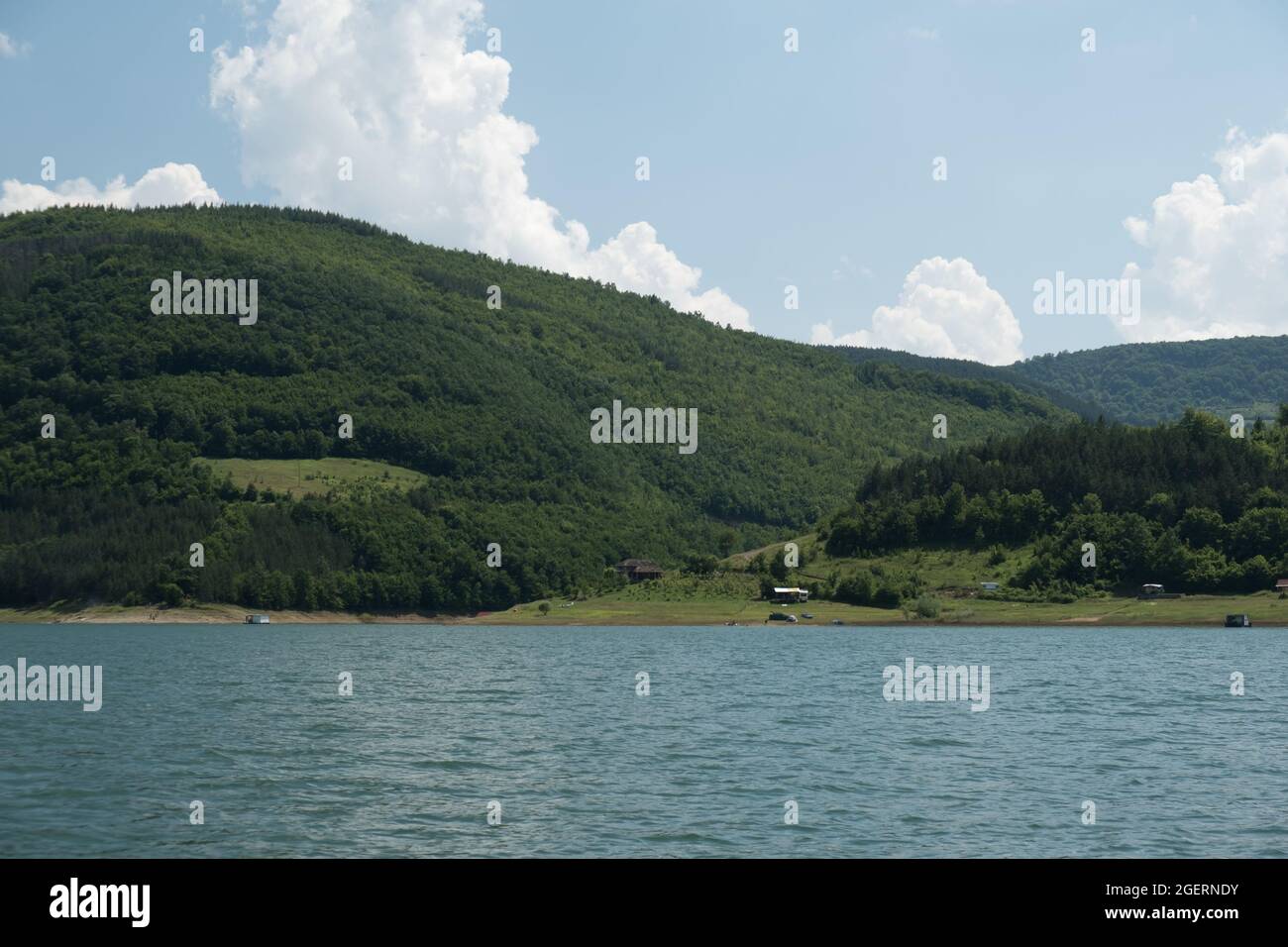 Bella Zavojsko jezozero (lago Zavoj) vista sull'acqua ondeggiante con montagne soleggiate e foreste verdi sull'altro lato e zattere in acqua Foto Stock