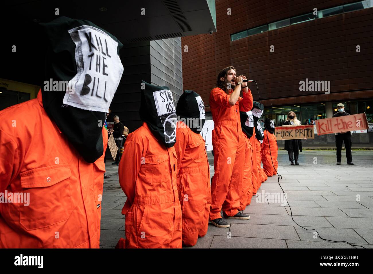 Manchester, Regno Unito. 21 Agosto 2021. I manifestanti vestiti con tute da caldaia arancioni si inginocchiano fuori dal Civil Justice Center. Le proteste in tutto il paese sono state organizzate a causa della proposta di legge di polizia, criminalità e condanna che, se approvata, introdurrebbe una nuova legislazione in materia di manifestazioni. Credit: Andy Barton/Alamy Live News Foto Stock