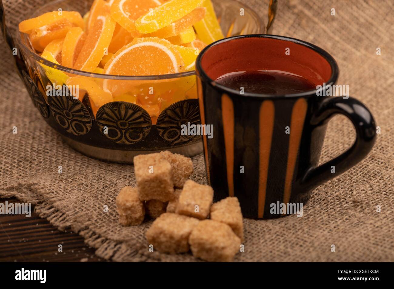 Fette di limone di marmellata multicolore in vaso di vetro, pezzi di zucchero di canna e una tazza di caffè, primo piano, fuoco selettivo Foto Stock